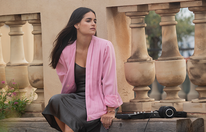 Andrea Lacoste sitting outdoors with a pink jacket and audio equipment.