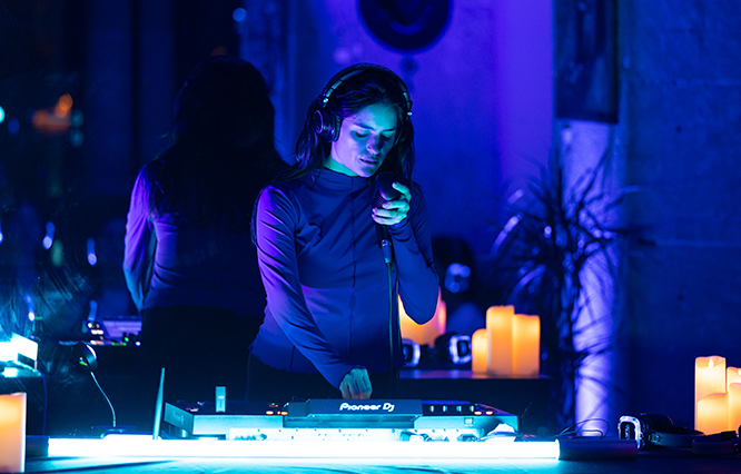 Andrea Lacoste DJing in a dimly lit room with blue lighting and candles.